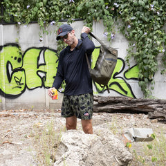 Man outdoors with Ranger Green GORUCK pack, camo shorts, in front of graffiti wall