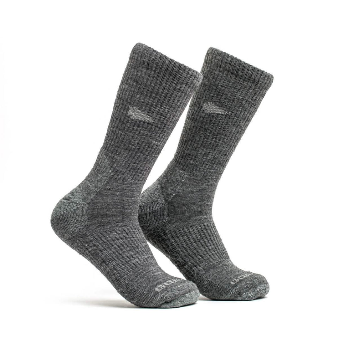 The GORUCK Merino Challenge Socks are gray, mid-calf, ribbed merino wool socks that stand upright on a white background, combining style and comfort.