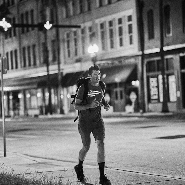 A man runs alone at night on a city street, wearing the Mackall 45 Black + Gum backpack with rugged durability and athletic clothes featuring a heritage suede upper.