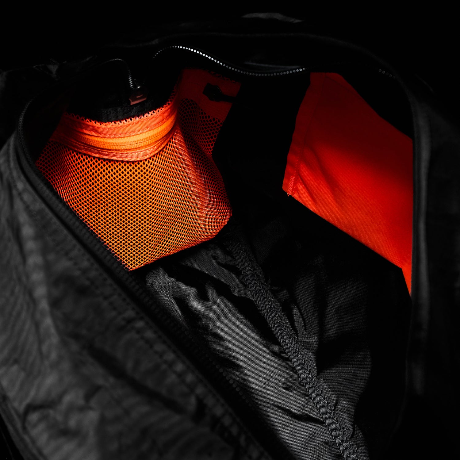 Open black bag with bright orange mesh pocket and fabric lining visible inside.