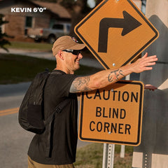 Man wearing GORUCK rucksack by caution blind corner sign outdoors, demonstrating fit at 6'0".