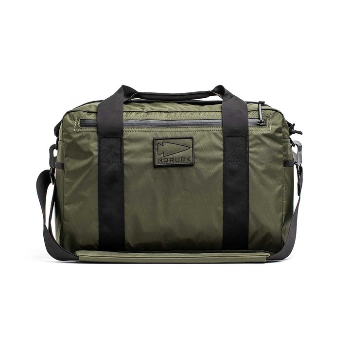 The Kit Bag - X-PAC in olive green features black straps, a front logo patch, and is made from durable X-PAC VX21 fabric, displayed against a white background.