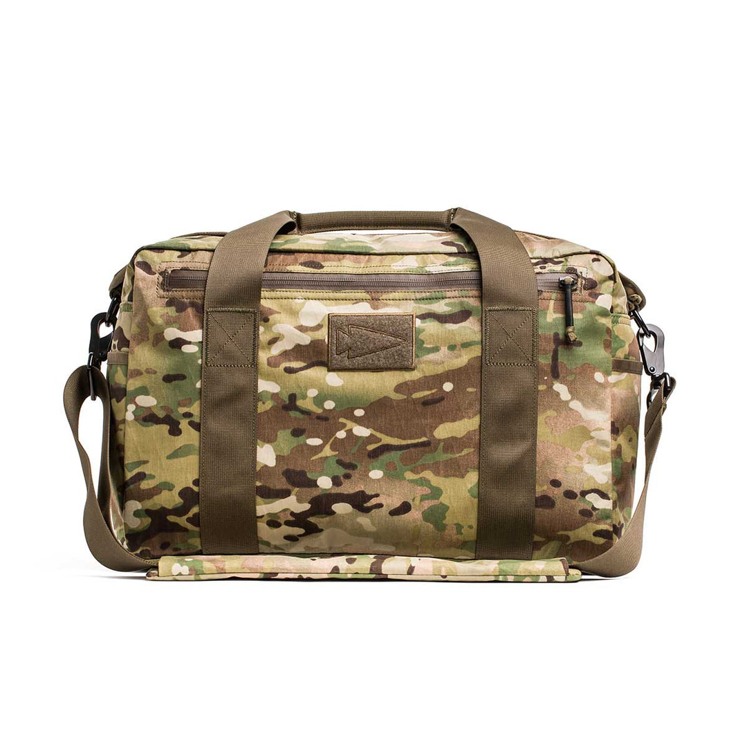 The Kit Bag - X-PAC, inspired by Special Forces gear, features camo print, olive green straps, and a shoulder strap. Shown against a white background.
