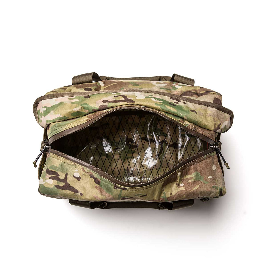 The Kit Bag - X-PAC is a camouflage duffel bag with a zippered opening, inspired by the classic aviator kit bag, and features an empty mesh pocket inside.