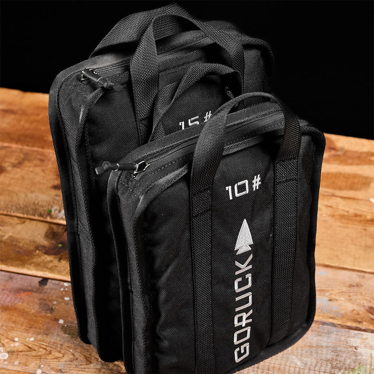 Two black GORUCK weight plates labeled 10 and 15 on a wooden surface.