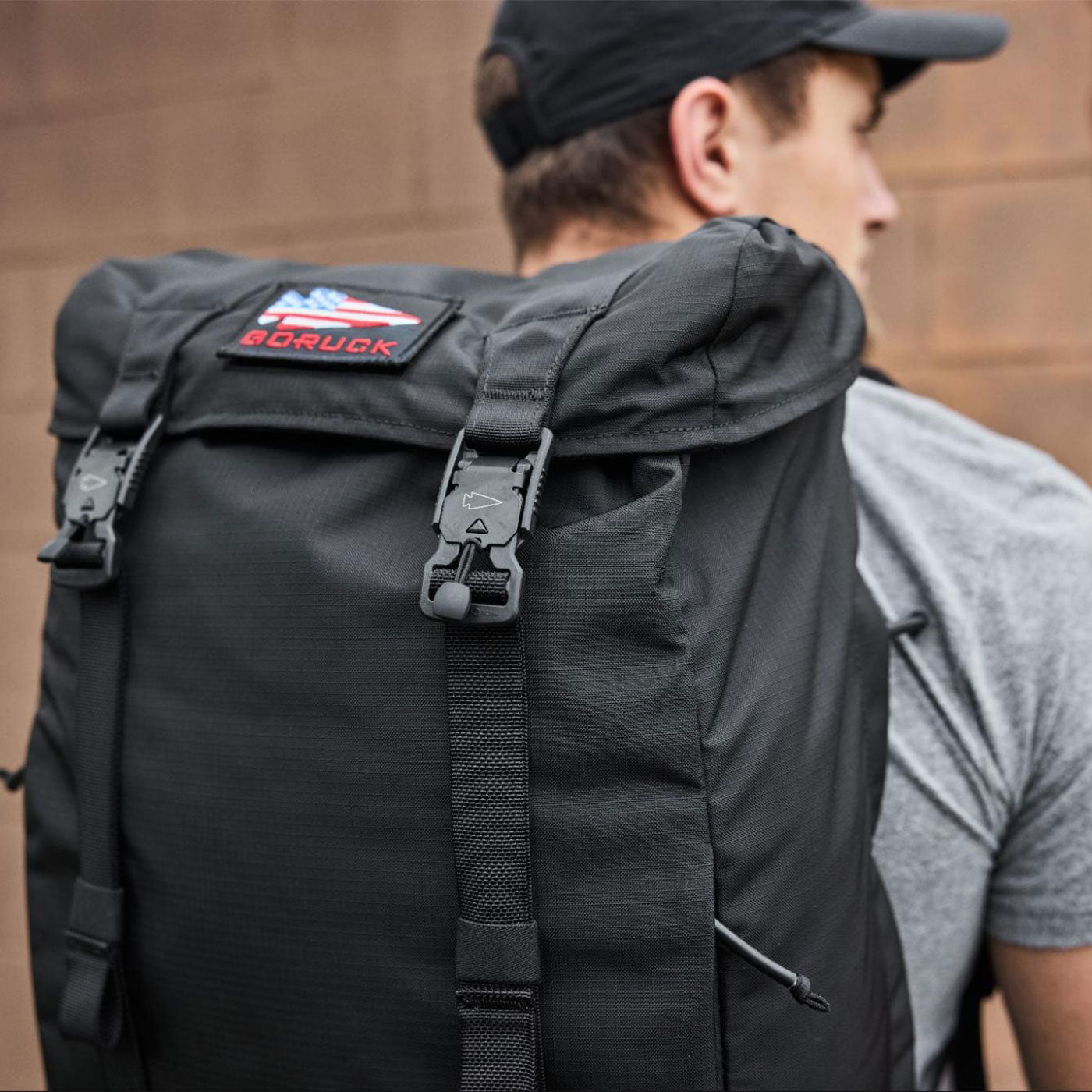 Person wearing a black GORUCK backpack and a black cap, facing away from the camera.