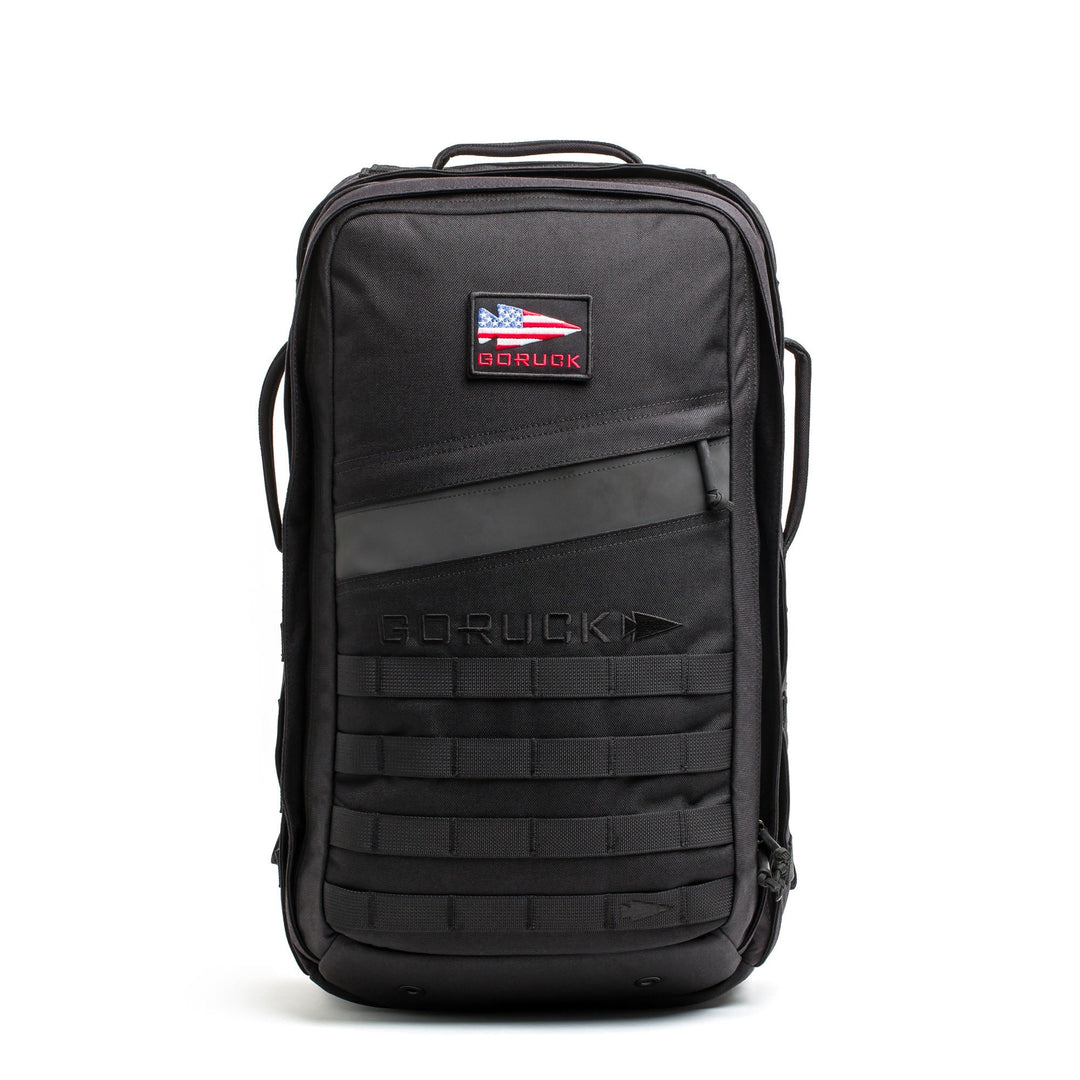 The Rucker - Long Range is a black backpack featuring an American flag patch, front handle, and lower front webbing—ideal as a comfortable rucksack for distance rucking or intense rucking events.