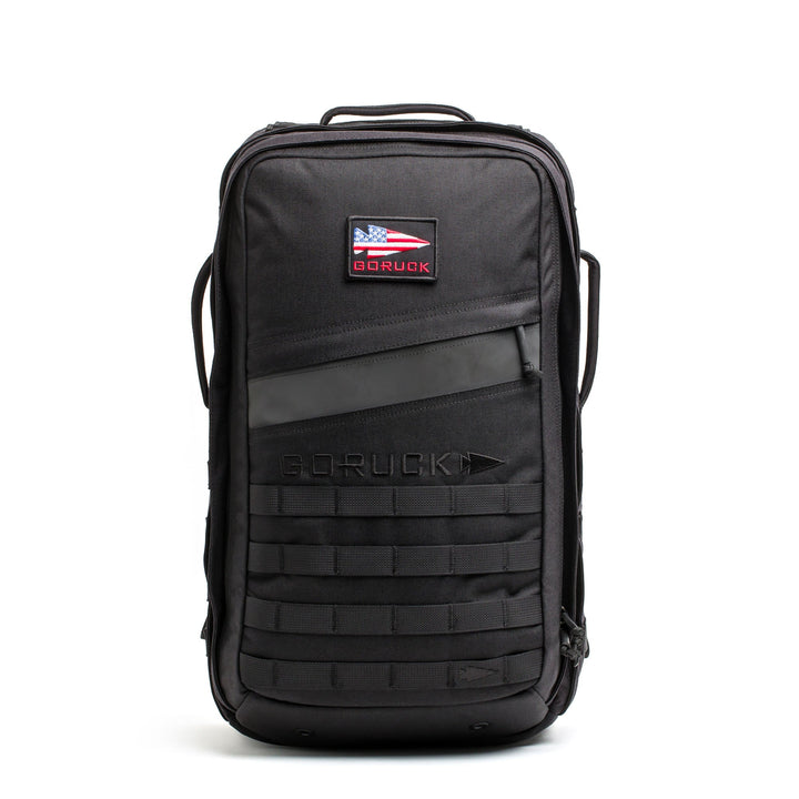 The Rucker - Long Range is a black backpack featuring an American flag patch, front handle, and lower front webbing—ideal as a comfortable rucksack for distance rucking or intense rucking events.