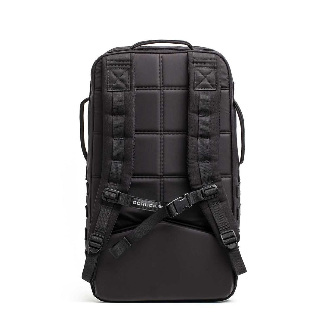 The Rucker - Long Range is a black backpack shown from the back, featuring padded shoulder straps and a sternum strap—built for distance rucking or events, and stands upright for easy access.