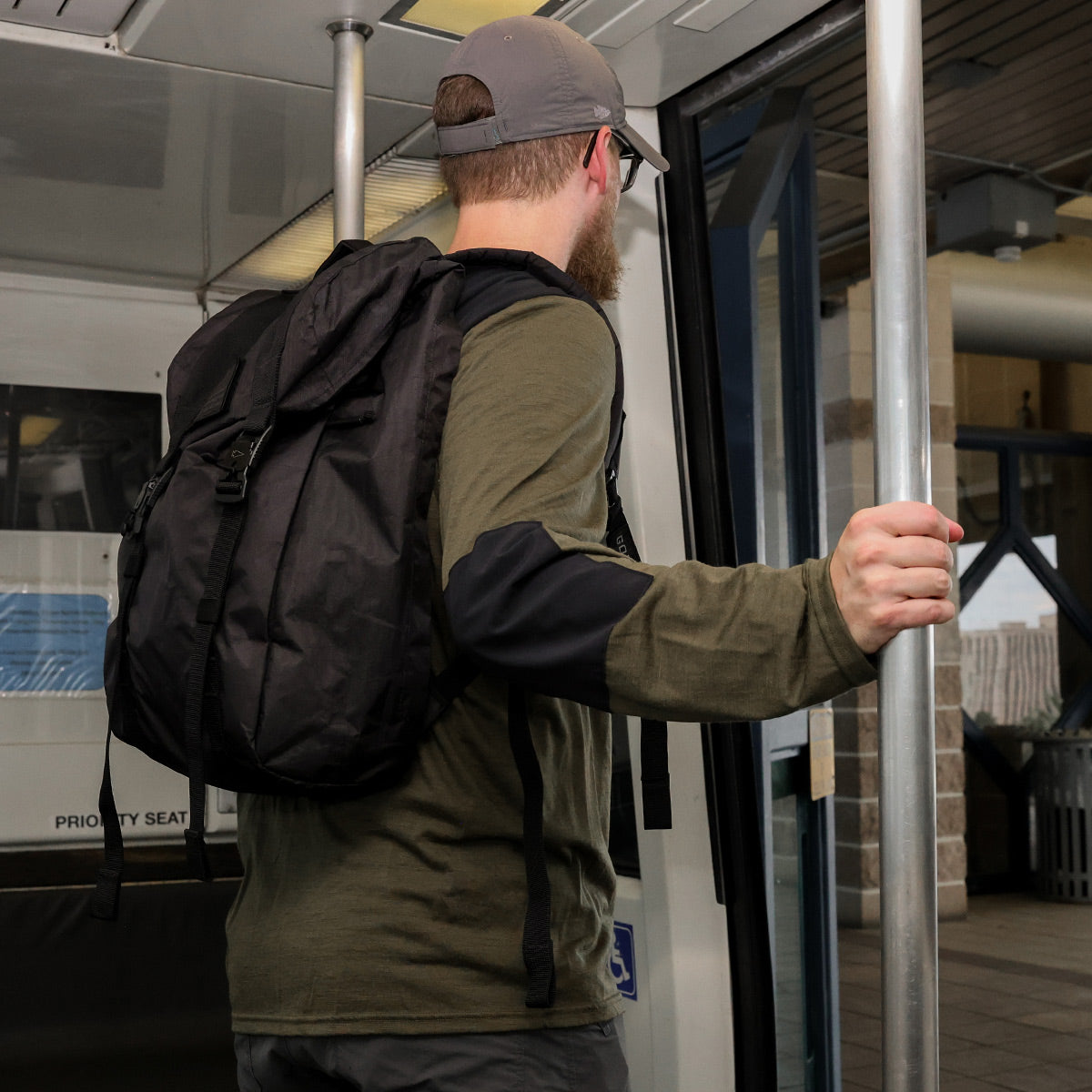 A man with a backpack and cap holds a pole while stepping onto a bus or train.