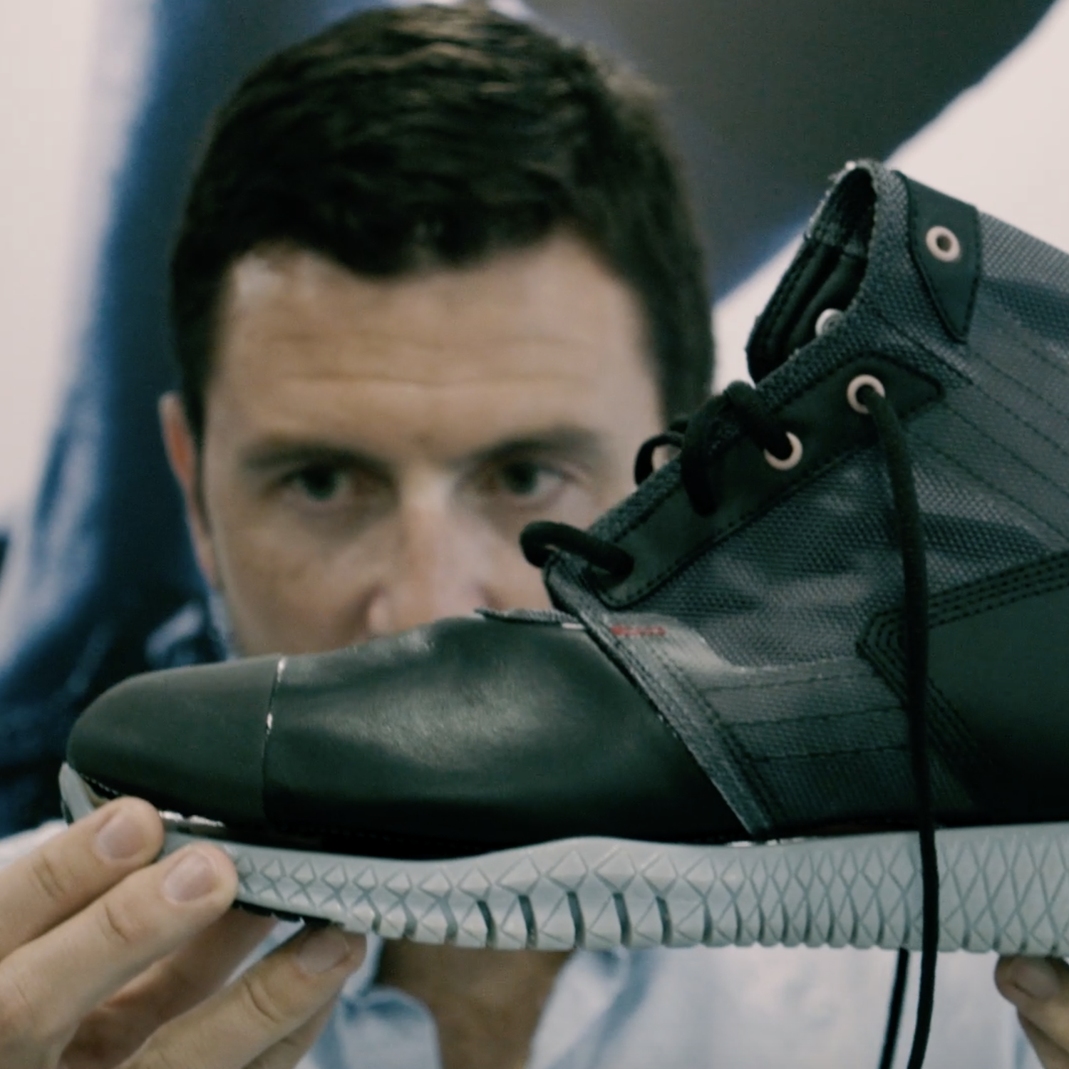 A man closely examines a black and gray sneaker, holding it up in front of his face.