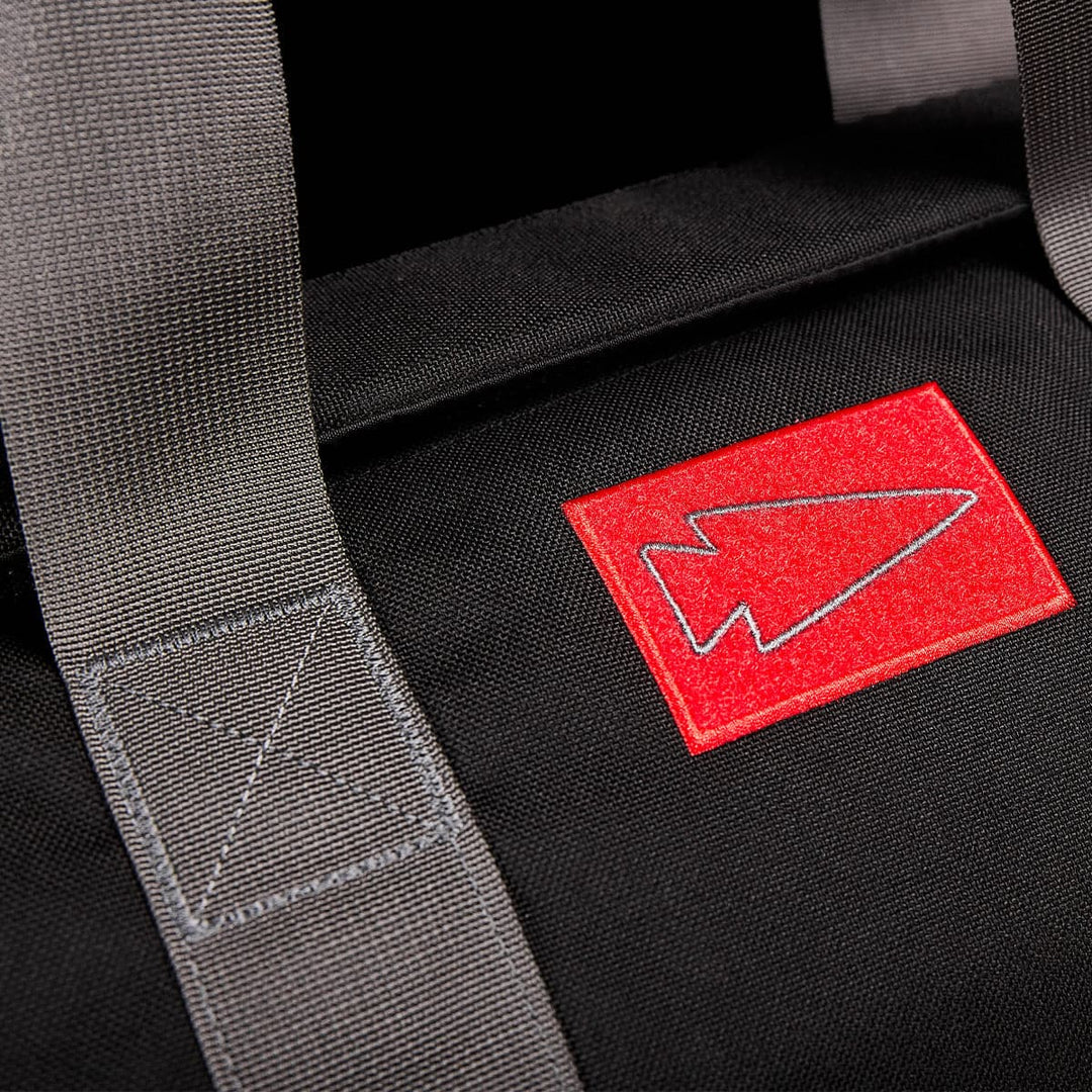 Close-up of the GORUCK black backpack, meticulously crafted from durable CORDURA fabric, showcasing a red arrow logo and gray straps—this versatile 38L design is ideal for use as a gym bag.