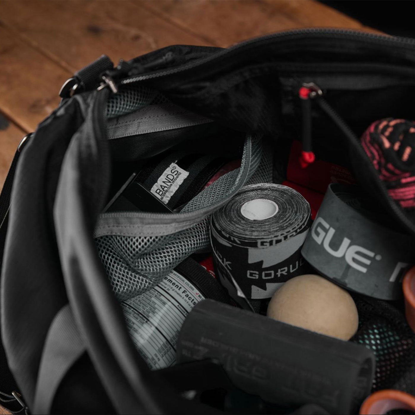 Open gym bag with resistance bands, tape, massage ball, and workout accessories on a wooden surface.
