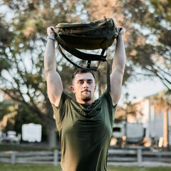 Man outdoors lifting rucksack overhead wearing olive GORUCK Tough Mesh Tee