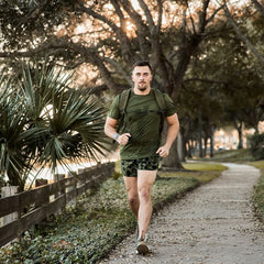 Man rucking in GORUCK olive Tough Mesh Tee outdoors, wearing rucksack on tree-lined path