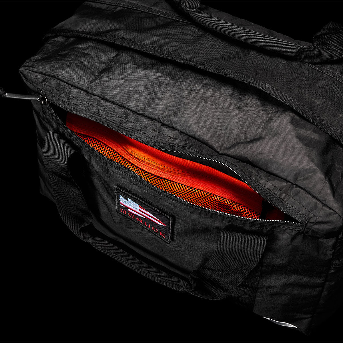 Black duffel bag with a partially open zipper, revealing an orange mesh interior pocket.