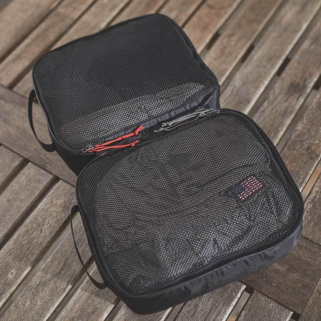 Two black GORUCK Packing Cubes—one open, one closed—crafted from ultra-light nylon and set on a wooden surface, ideal for keeping your travel gear organized.