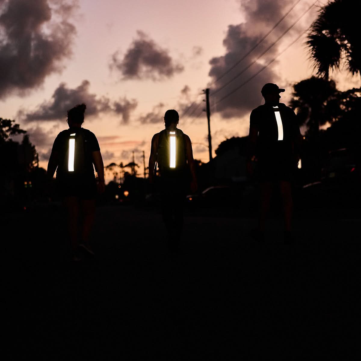 Three people rucking at sunset with GORUCK backpacks featuring reflective strips.