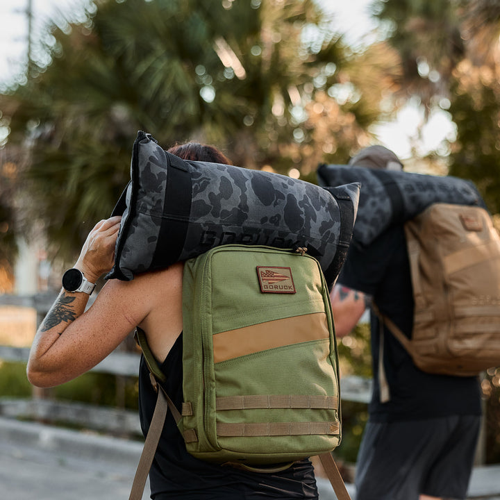 Two people hike outdoors with GORUCK Simple Training Sandbags on their shoulders, showing you can take your fitness anywhere—no gym required.