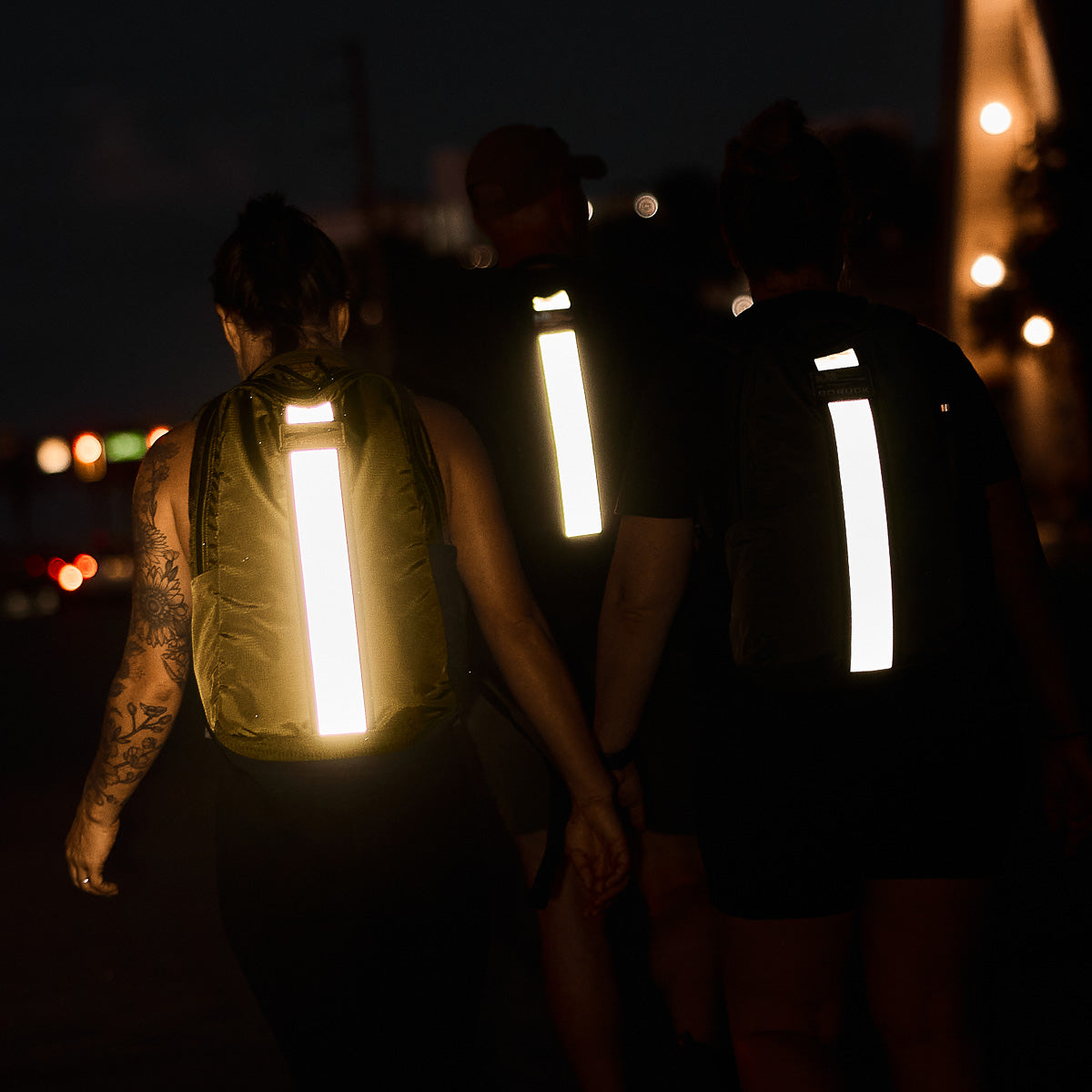 Three people walking at night with backpacks featuring bright reflective strips for visibility.