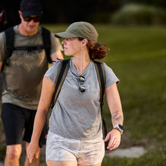 Woman rucking outdoors wearing GORUCK gear, backpack, and cap on grassy path