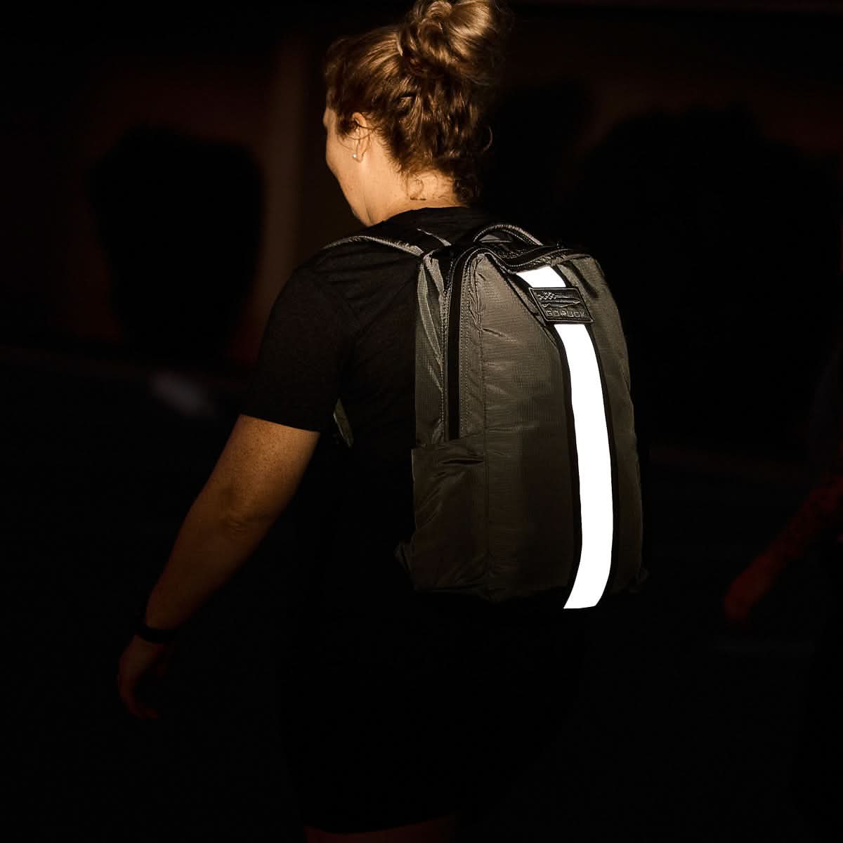 Person wearing GORUCK backpack with reflective stripe at night, rucking gear for safety.