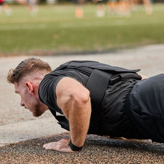 A man does push-ups outdoors on a track, intensifying his workout by wearing a weight vest loaded with Curved Ruck Plates for added resistance.