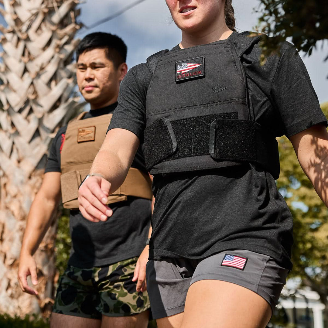 Two people wearing athletic clothing and Curved Ruck Plates walk outdoors under sunny skies.