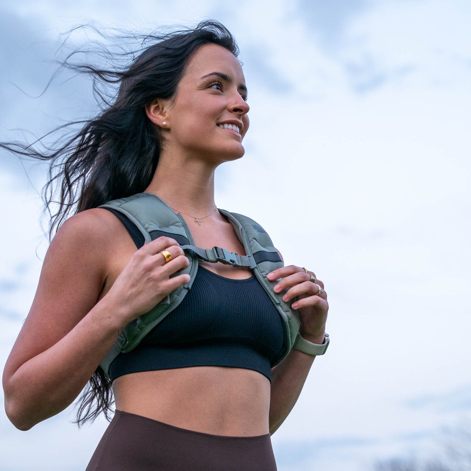 Woman outdoors in a Spy Ruck | Women's Weighted Vest, gazing to the side as the wind sweeps her hair beneath a cloudy sky.