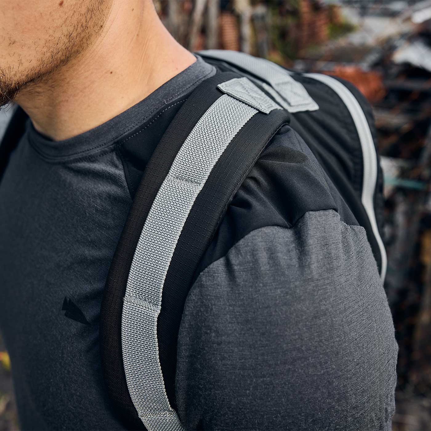 Close-up of a person wearing a grey shirt and carrying a black and grey backpack over their shoulder.