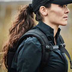 Woman outdoors wearing black GORUCK backpack and cap, showcasing rugged rucking gear