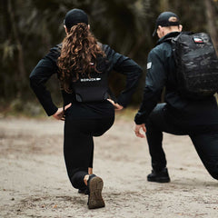 Two people wearing GORUCK gear performing outdoor lunges on a dirt trail.