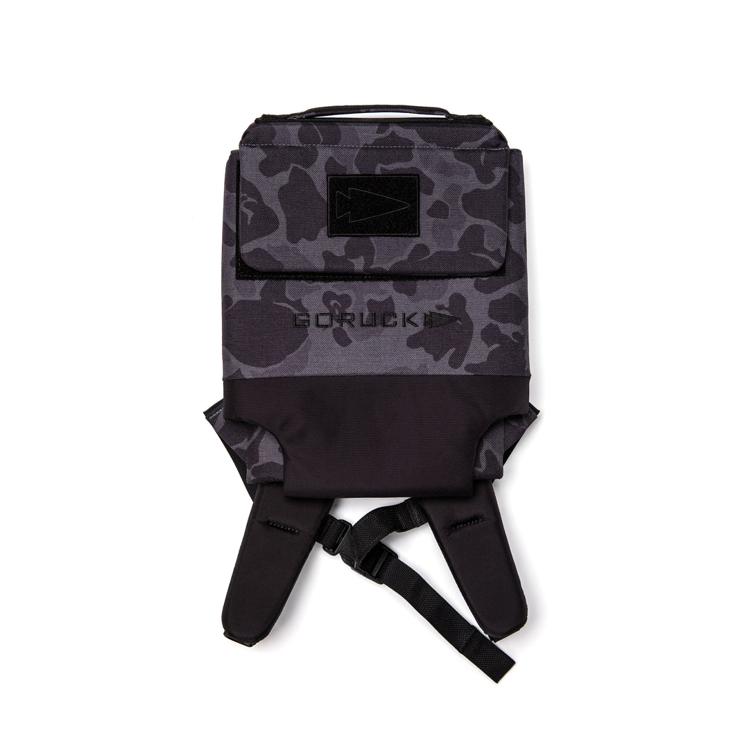 The GORUCK Ruck Plate Carrier 3.0 in black and gray camouflage features a flap closure, front pocket, ergonomic lumbar support, and displays the "GORUCK" logo, as seen from above.