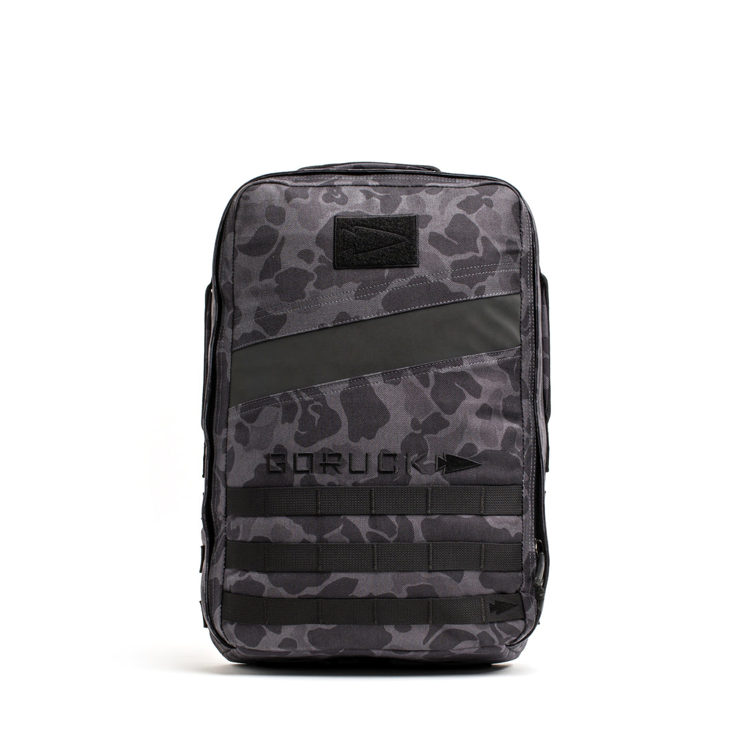 The GORUCK Rucker 4.0 backpack in black and grey camo features the GORUCK logo, front webbing, and a diagonal black stripe—ideal for rucking adventures.