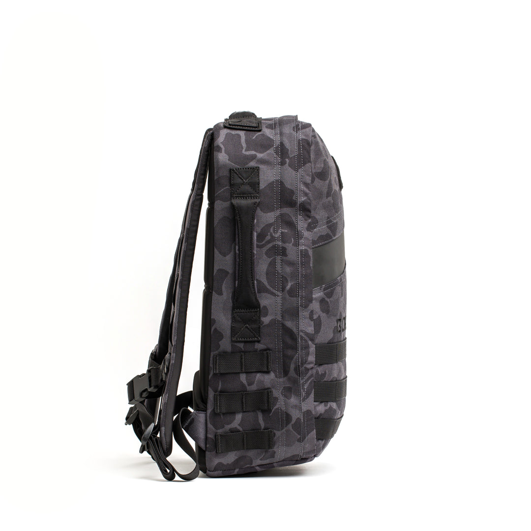 The GORUCK Rucker 4.0, shown side-on against a white background, features gray camouflage, multiple straps, and a side handle—ideal for rucking or outdoor adventures.