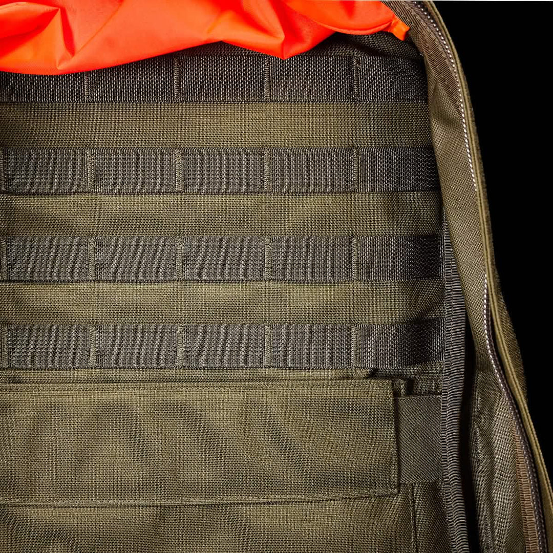 Close-up of the inside of a green GORUCK GR2 backpack reveals horizontal webbing and an orange lining, making it a rugged, carry-on compliant travel rucksack.