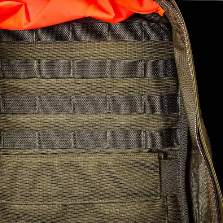 Close-up of the inside of a green GORUCK GR2 backpack reveals horizontal webbing and an orange lining, making it a rugged, carry-on compliant travel rucksack.