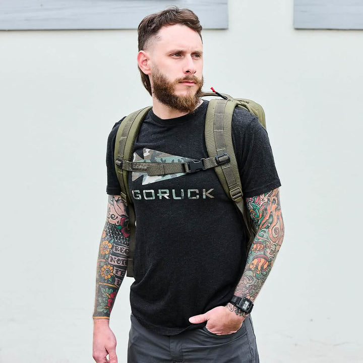 Tattooed bearded man outdoors with a backpack, wearing a black GORUCK t-shirt, ready for adventure with his carry-on compliant GORUCK GR2 Special Forces backpack.