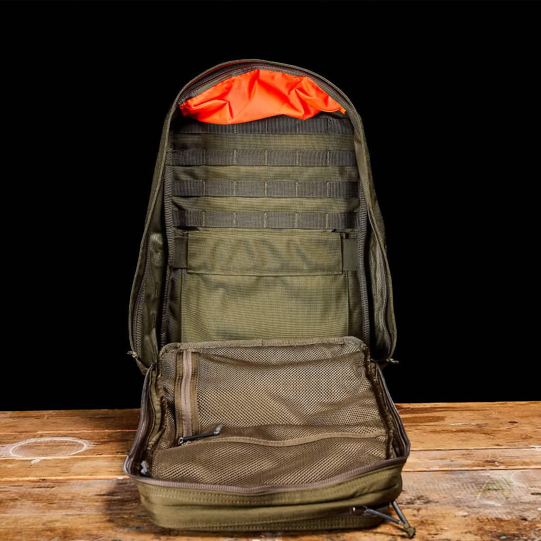 The GORUCK GR2, an open green travel rucksack with mesh pockets and orange interior lining, sits on a wooden surface.