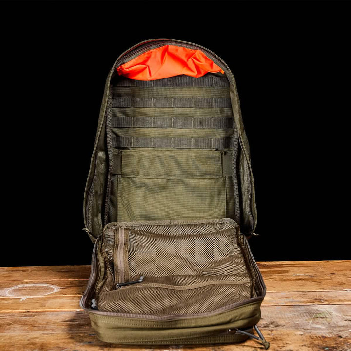 The GORUCK GR2, an open green travel rucksack with mesh pockets and orange interior lining, sits on a wooden surface.