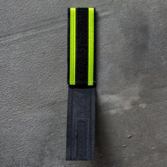 A Reflective Ruck Band from GORUCK, featuring a striking combination of black and neon yellow, sits on a gray surface, making it perfect for nighttime visibility. This versatile accessory is ideal for any situation requiring enhanced safety.