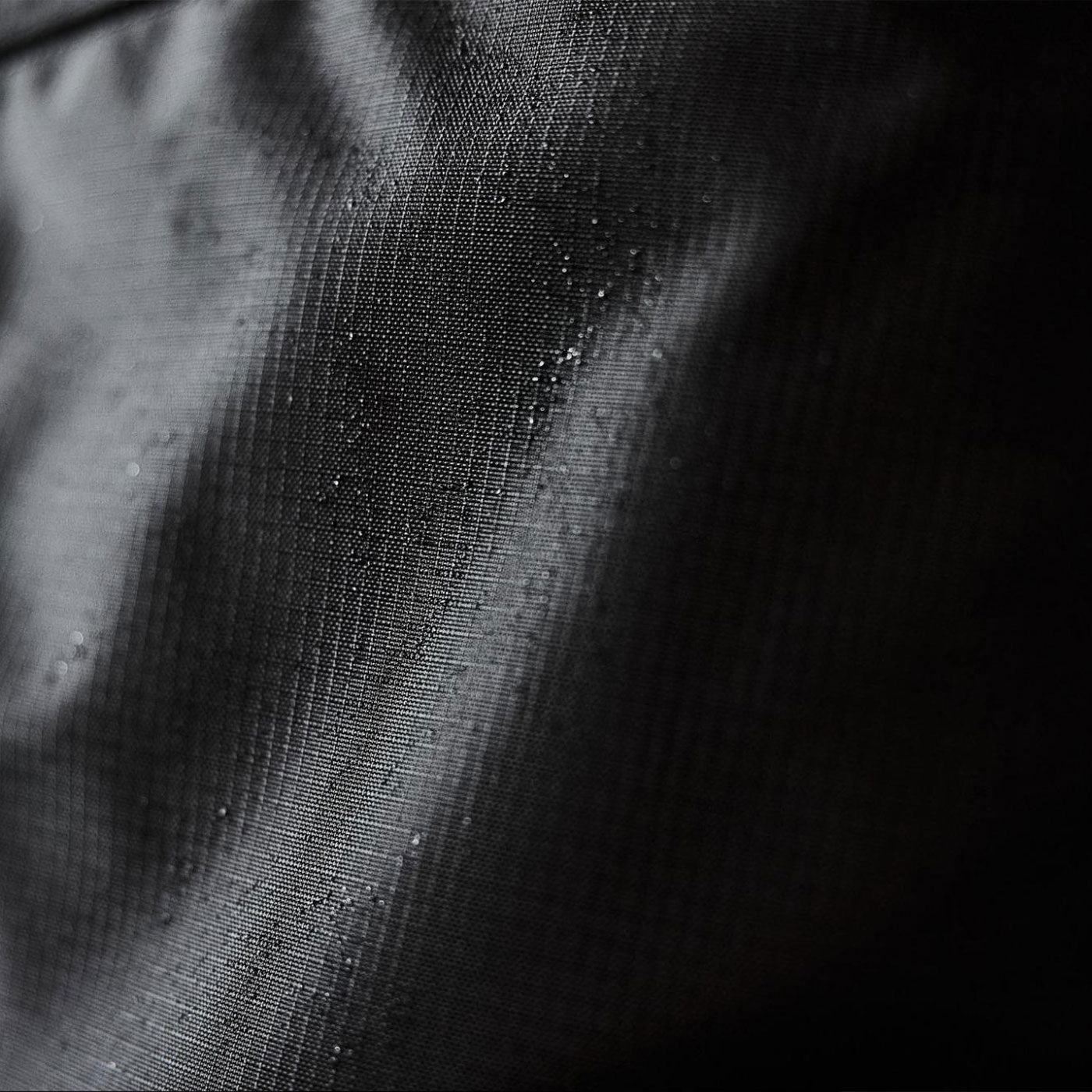 Close-up of dark fabric with a subtle grid texture and small water droplets on its surface.
