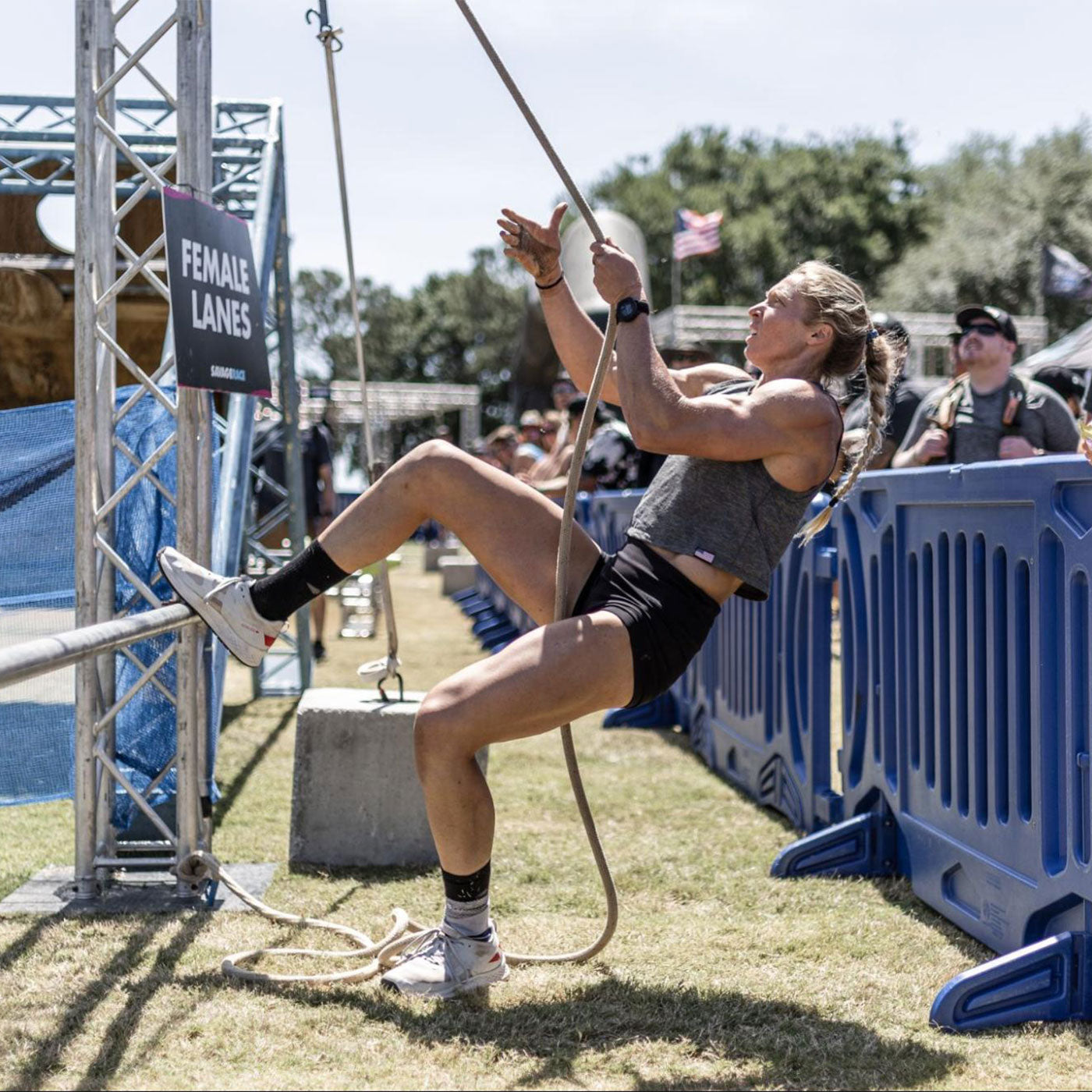 Athletic woman climbs a rope in an outdoor competition near a sign labeled 