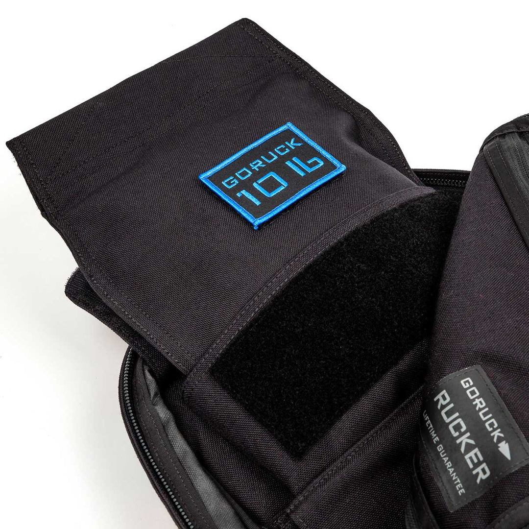 Open black backpack with blue "GORUCK 10LB" patch and inner Velcro—ideal for carrying your GORUCK Ruck Sandbag - 10LB (4.5KG) in any workout.