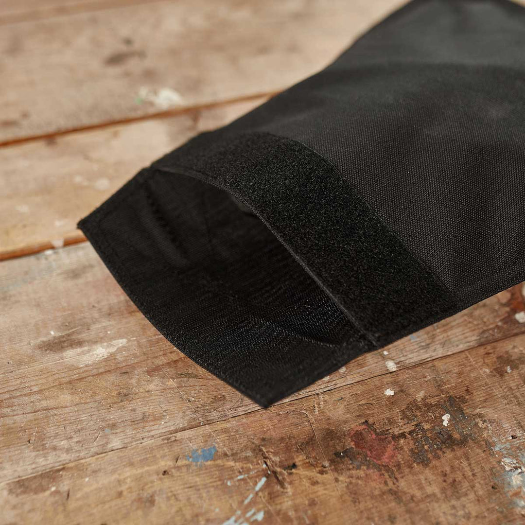 A close-up of a black fabric GORUCK Ruck Sandbag - 10LB (4.5KG) sleeve with a velcro closure, resting on a worn wooden surface.