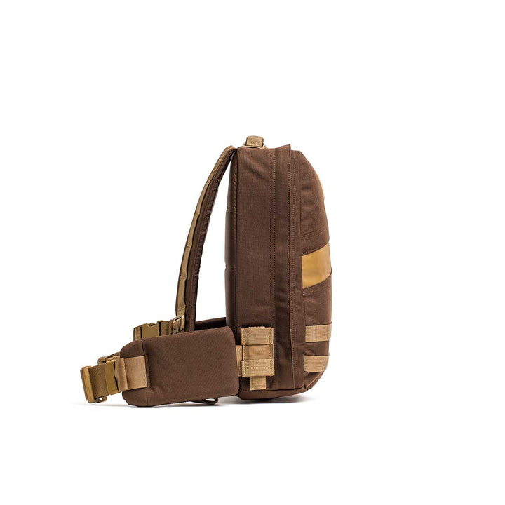 The GORUCK Rucker 4.0 is a brown sling rucking backpack with an adjustable strap, tan accents, and multiple compartments, shown from the side.