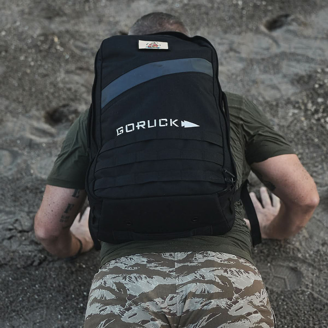 A person using the Ruck Clubs Starter Kit - Light from GORUCK crawls on sandy ground in a military-style exercise, highlighting endurance and strength.