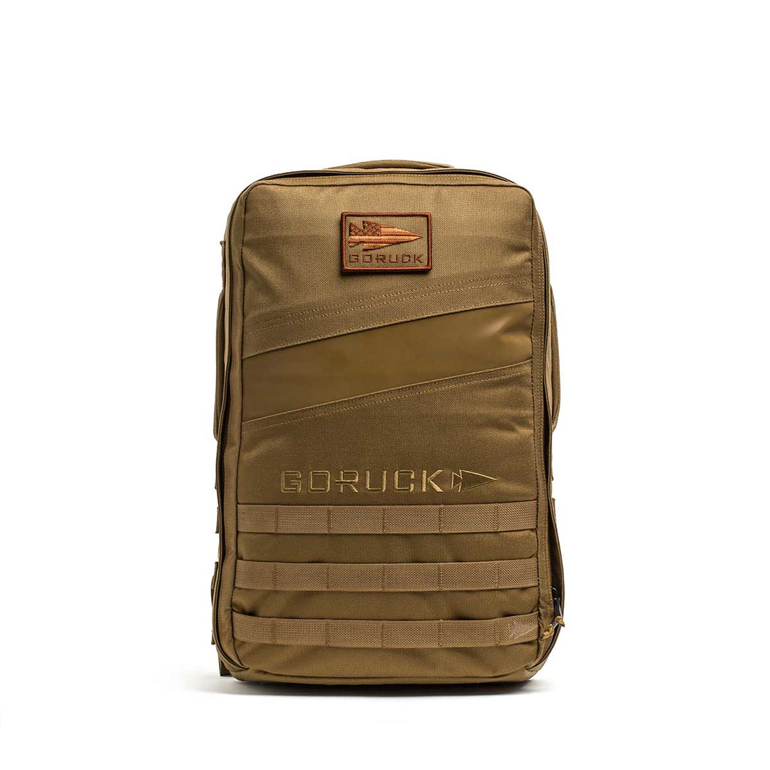 The GORUCK Rucker 4.0 backpack in tan features a front patch, diagonal accent, multiple horizontal webbing straps, and is built for rucking—compatible with Ruck Plates for extra training challenge.