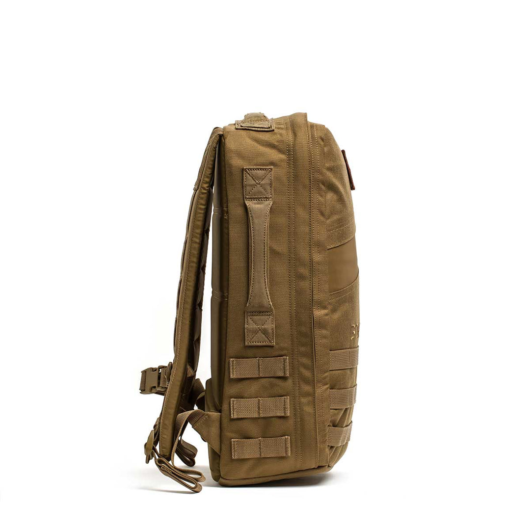 Side view of the GORUCK Rucker 4.0 backpack in brown, featuring MOLLE webbing and padded shoulder straps; designed for rucking and compatible with ruck plates, standing upright.