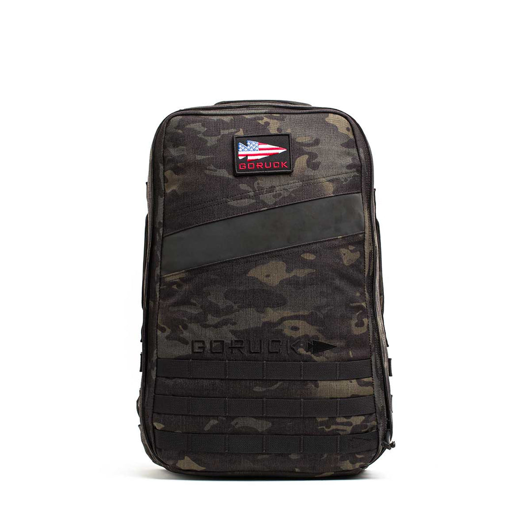 The GORUCK Rucker 4.0 backpack in black camo features an American flag patch and bold "GORUCK" branding, designed for use with Ruck Plates, shown against a white background.